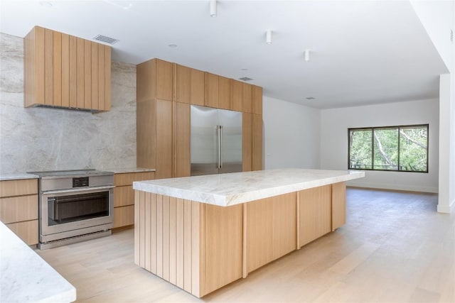 kitchen with built in refrigerator, stove, a center island, light hardwood / wood-style floors, and light brown cabinetry