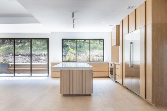 kitchen featuring light brown cabinetry, stainless steel built in fridge, a kitchen island, and light hardwood / wood-style flooring