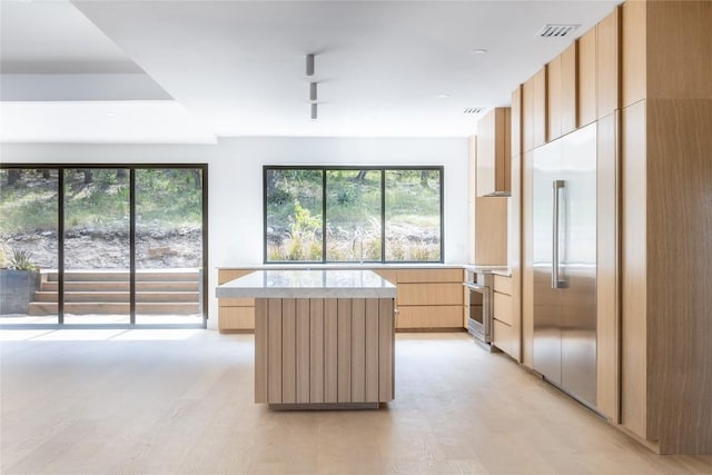 kitchen with modern cabinets, light brown cabinetry, visible vents, a kitchen island, and light countertops