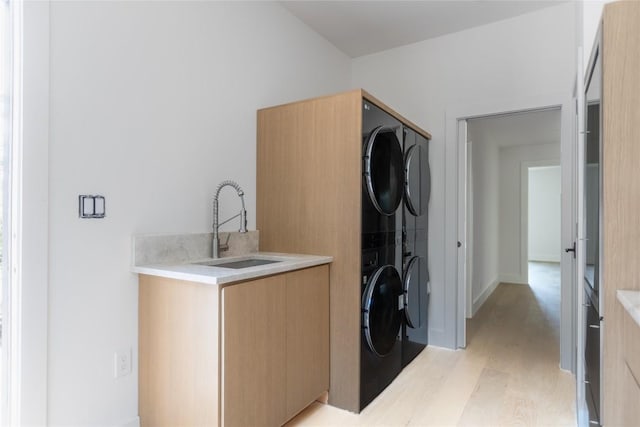 laundry area featuring light wood-type flooring, stacked washer and clothes dryer, a sink, and cabinet space