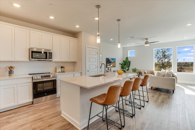 kitchen with stainless steel appliances, white cabinetry, sink, and a center island with sink