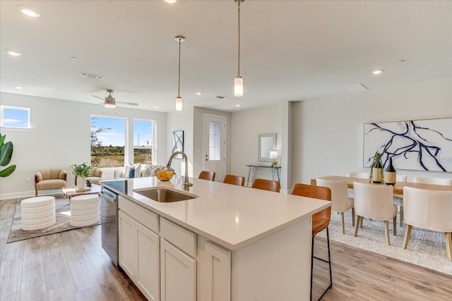 kitchen featuring sink, dishwasher, hanging light fixtures, an island with sink, and white cabinets