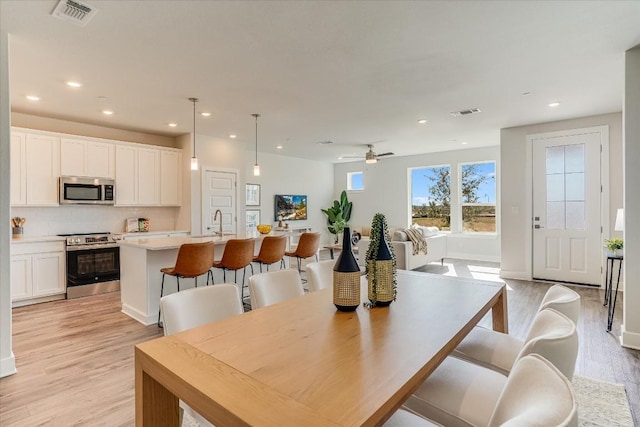 dining space with ceiling fan, sink, and light wood-type flooring