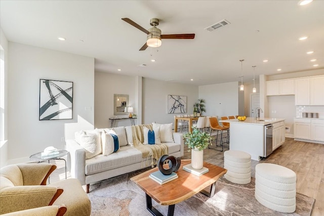 living room with ceiling fan, sink, and light wood-type flooring