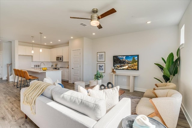 living room with ceiling fan, sink, and light hardwood / wood-style flooring