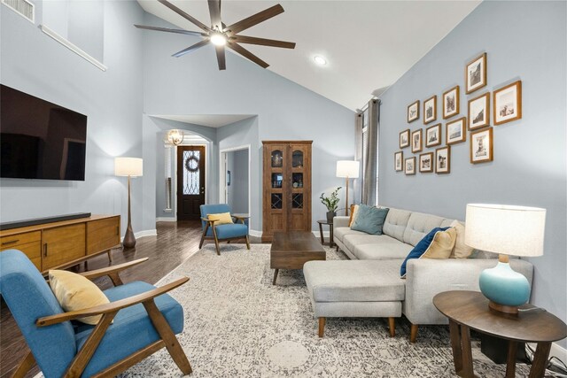 living room with visible vents, high vaulted ceiling, ceiling fan with notable chandelier, wood finished floors, and baseboards