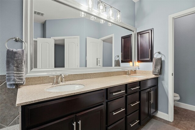 bathroom featuring double vanity, visible vents, toilet, and a sink