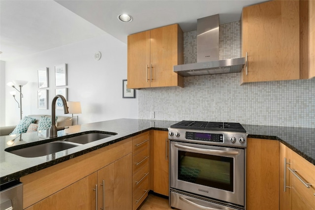 kitchen featuring dark stone countertops, sink, stainless steel gas stove, and wall chimney exhaust hood