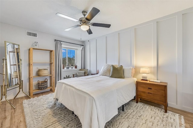 bedroom with light wood-style floors, visible vents, a decorative wall, and a ceiling fan