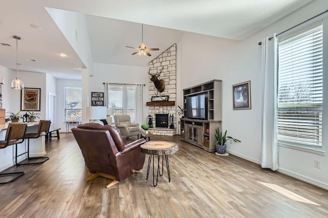 living room featuring lofted ceiling, a stone fireplace, wood-type flooring, and ceiling fan