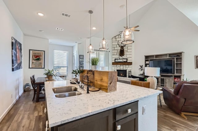 kitchen featuring a stone fireplace, sink, decorative light fixtures, a center island with sink, and dark hardwood / wood-style flooring