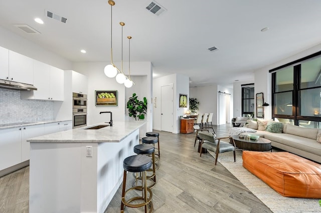 kitchen with pendant lighting, white cabinetry, an island with sink, sink, and decorative backsplash