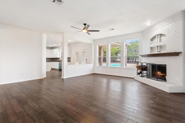 unfurnished living room featuring a brick fireplace, dark wood-type flooring, and ceiling fan