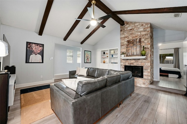 living room featuring built in features, ceiling fan, vaulted ceiling with beams, a stone fireplace, and light wood-type flooring