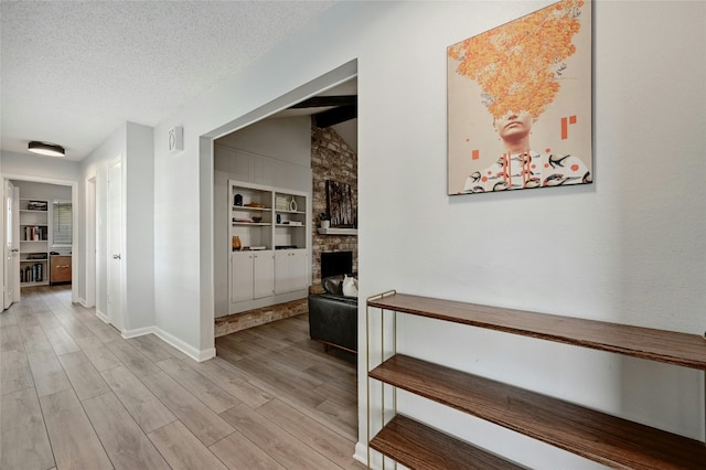 hallway featuring lofted ceiling, light hardwood / wood-style flooring, built in features, and a textured ceiling