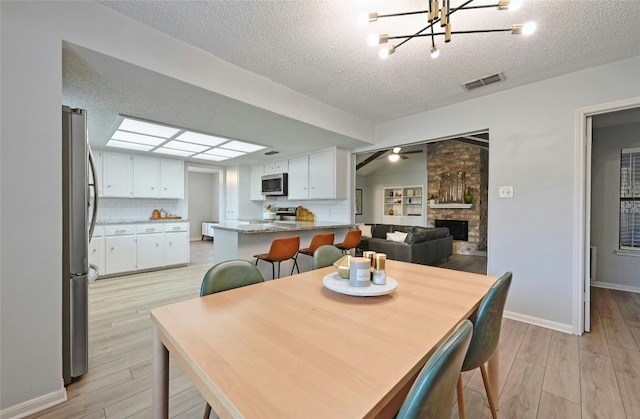 dining room with a textured ceiling, a fireplace, ceiling fan, and light wood-type flooring