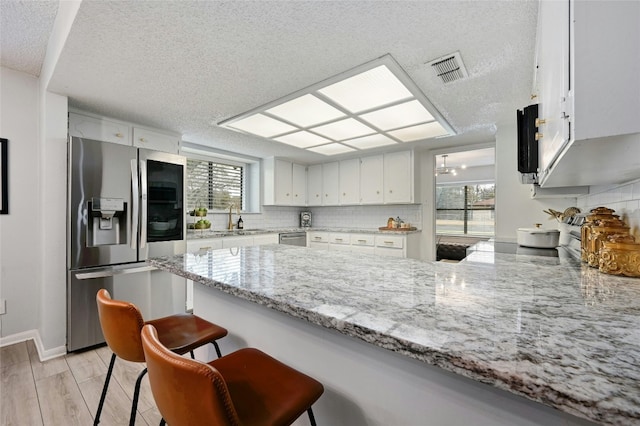 kitchen featuring stainless steel appliances, light stone countertops, a textured ceiling, white cabinets, and kitchen peninsula