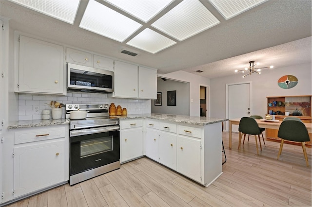 kitchen with stainless steel appliances, light stone counters, white cabinets, decorative backsplash, and kitchen peninsula