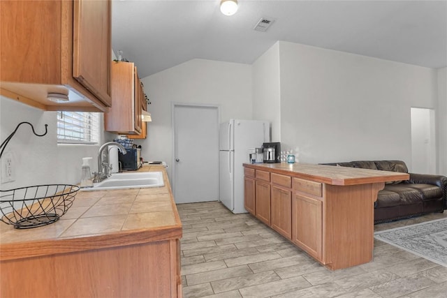 kitchen featuring a breakfast bar, tile countertops, sink, white fridge, and kitchen peninsula