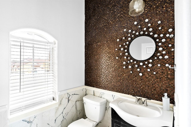 half bathroom with a wainscoted wall, vanity, toilet, and tile walls