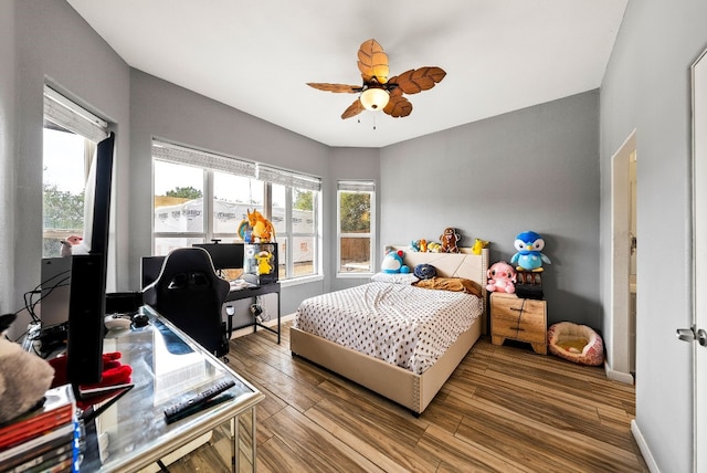 bedroom with a ceiling fan, multiple windows, baseboards, and wood finished floors