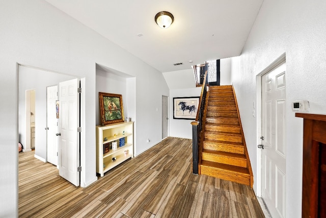 stairs featuring visible vents, vaulted ceiling, and wood finished floors