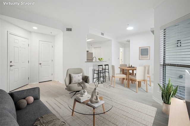 living room with ornamental molding, sink, and light wood-type flooring