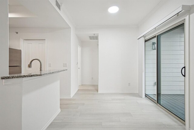 corridor featuring crown molding, a sink, visible vents, and light wood-style floors