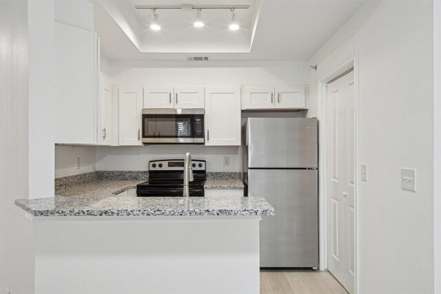 kitchen featuring light stone counters, a tray ceiling, kitchen peninsula, stainless steel appliances, and white cabinets