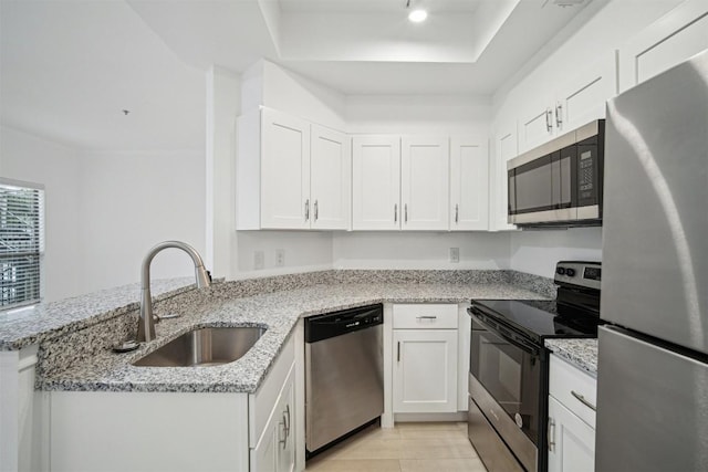 kitchen featuring light stone counters, stainless steel appliances, white cabinets, a sink, and a peninsula