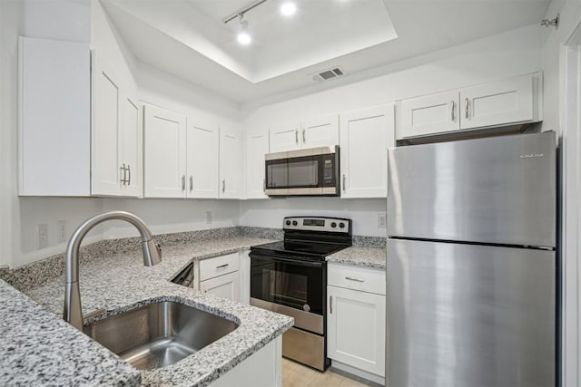 kitchen featuring a raised ceiling, sink, white cabinets, stainless steel appliances, and light stone countertops