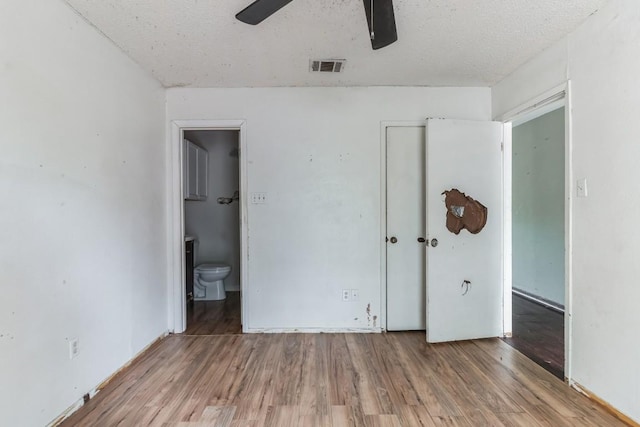 unfurnished bedroom with ensuite bath, a textured ceiling, ceiling fan, and light wood-type flooring