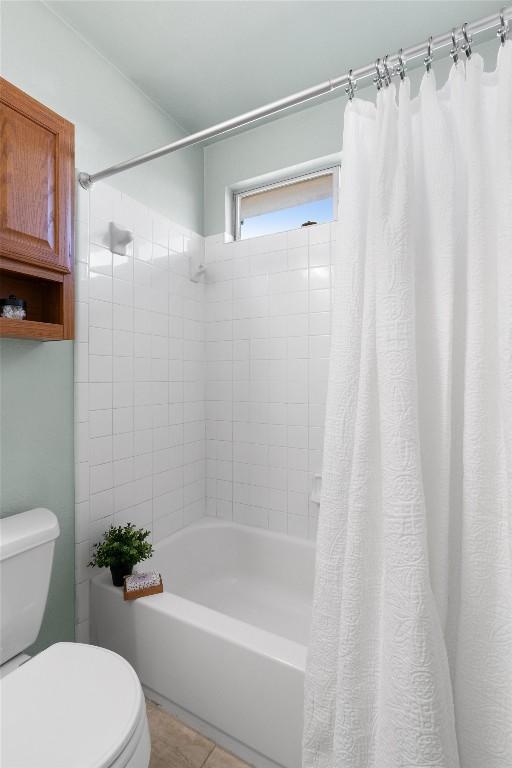 bathroom featuring shower / bathtub combination with curtain, tile patterned floors, and toilet