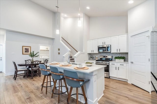 kitchen with white cabinetry, decorative light fixtures, stainless steel appliances, and a towering ceiling