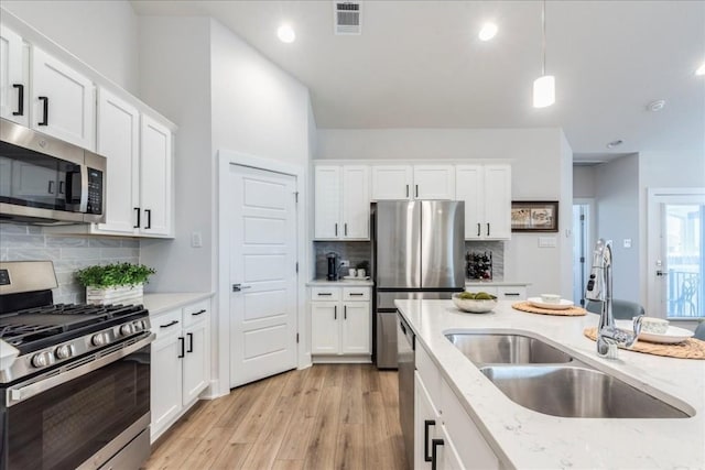 kitchen with appliances with stainless steel finishes, pendant lighting, sink, white cabinets, and light stone counters