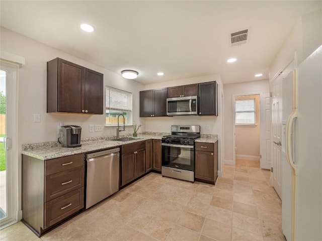 kitchen with stainless steel appliances, light stone countertops, sink, and dark brown cabinets