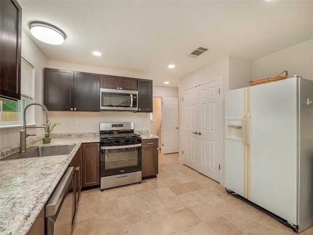 kitchen with stainless steel appliances, light stone countertops, sink, and dark brown cabinets