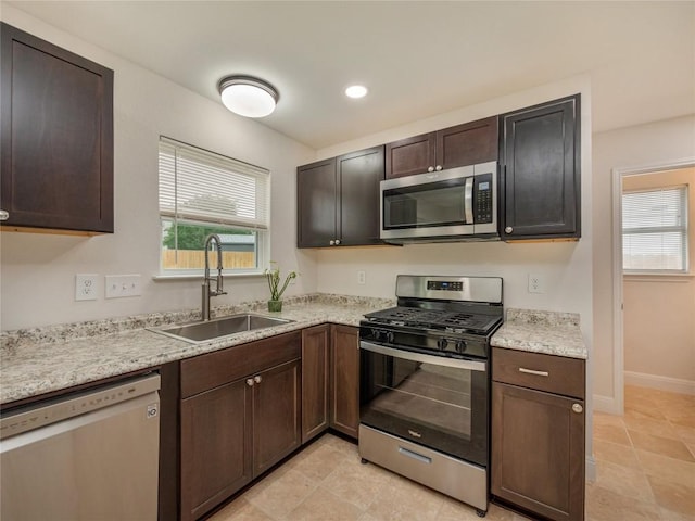 kitchen featuring sink, light tile patterned floors, stainless steel appliances, dark brown cabinetry, and light stone counters