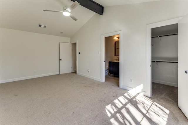 unfurnished bedroom with ensuite bath, a spacious closet, lofted ceiling with beams, light carpet, and a closet