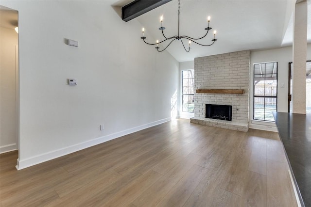 unfurnished living room with beam ceiling, hardwood / wood-style floors, a brick fireplace, and a notable chandelier