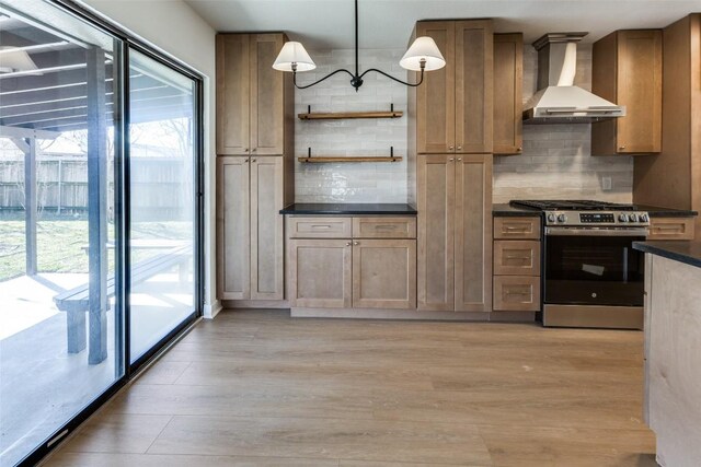 kitchen featuring wall chimney exhaust hood, tasteful backsplash, hanging light fixtures, stainless steel range with gas stovetop, and light hardwood / wood-style floors