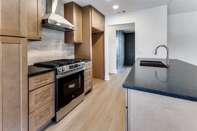 kitchen featuring sink, stainless steel gas range, tasteful backsplash, wall chimney exhaust hood, and light wood-type flooring