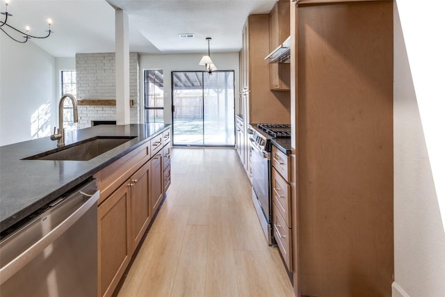 kitchen with appliances with stainless steel finishes, pendant lighting, a fireplace, sink, and light hardwood / wood-style floors