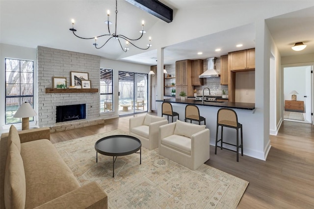 living room featuring vaulted ceiling with beams, light hardwood / wood-style floors, a chandelier, and a brick fireplace