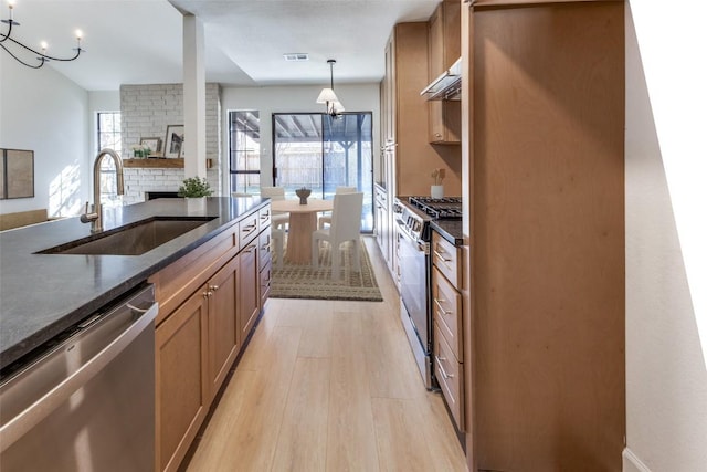 kitchen with appliances with stainless steel finishes, a stone fireplace, pendant lighting, sink, and light wood-type flooring