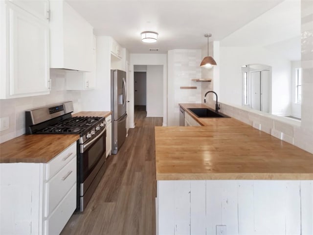 kitchen featuring sink, butcher block countertops, decorative light fixtures, appliances with stainless steel finishes, and kitchen peninsula