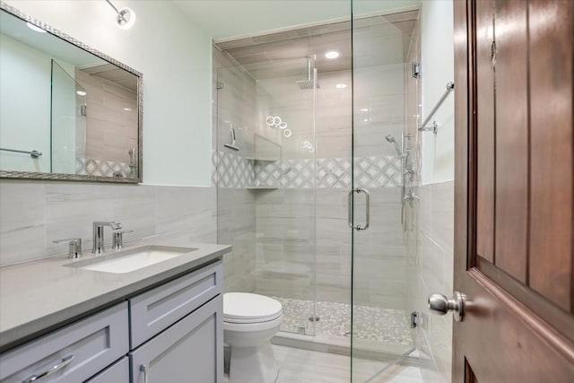 bathroom with vanity, toilet, a shower with shower door, and tile walls