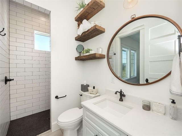 bathroom featuring a tile shower, vanity, and toilet