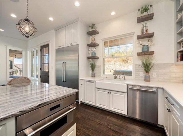 kitchen with sink, hanging light fixtures, appliances with stainless steel finishes, decorative backsplash, and white cabinets