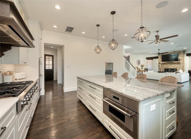 kitchen with custom exhaust hood, white cabinetry, decorative light fixtures, a kitchen island, and light stone countertops